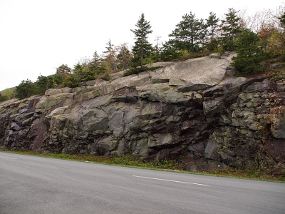 [Jagged rock pieces jutting from the hillside which is topped with smaller evergreens. The road is in the foreground.]